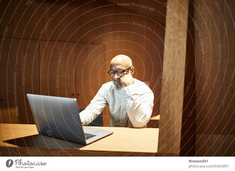 Porträt eines reifen Mannes, der an einem Laptop an einem Arbeitsbereich mit Holzverkleidung arbeitet arbeiten Wandverkleidung Erwachsener Mensch Verkleidung