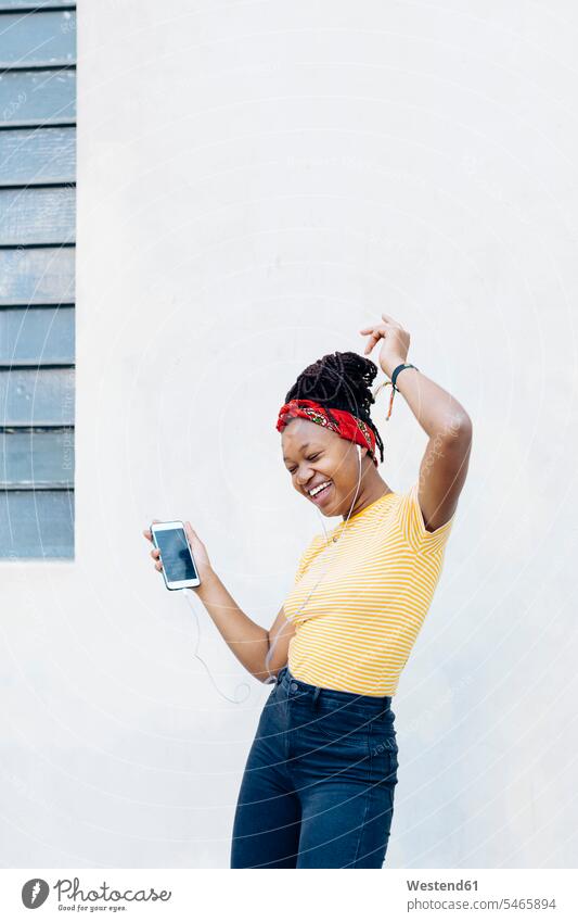 Junge Frau, die mit Kopf- und Ohrhörern Musik hört und vor einer weißen Wand singt und tanzt T-Shirts Handies Handys Mobiltelefon Mobiltelefone Displays hoeren