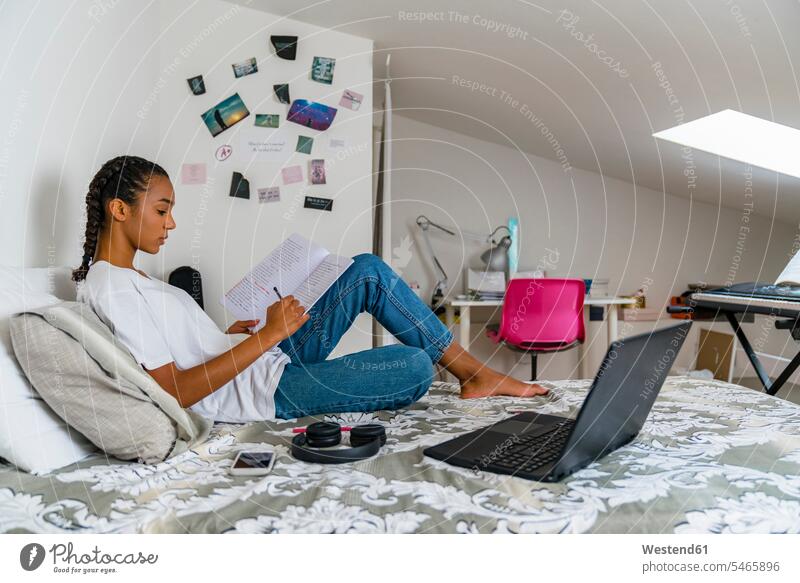Teenager-Mädchen schreibt zu Hause auf dem Bett sitzend in ein Schulheft Farbaufnahme Farbe Farbfoto Farbphoto Innenaufnahme Innenaufnahmen innen drinnen Tag