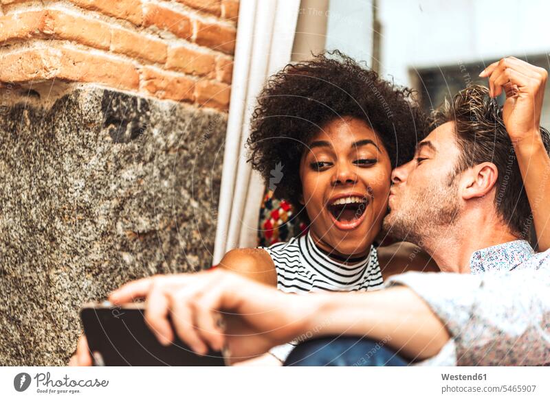 Nahaufnahme eines Mannes, der seine fröhliche Freundin küsst, während er im Café Selfie mitnimmt Farbaufnahme Farbe Farbfoto Farbphoto Innenaufnahme