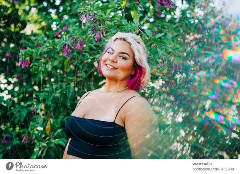 Lächelnde, grossgewachsene Frau steht in der Nähe einer blühenden Pflanze im Freien Farbaufnahme Farbe Farbfoto Farbphoto Außenaufnahme außen draußen Tag