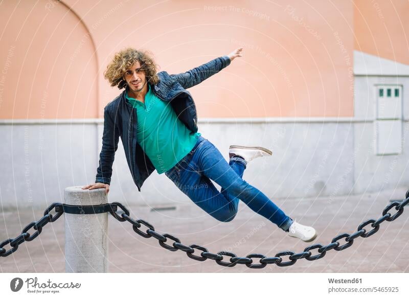 Porträt eines lächelnden jungen Mannes, der über eine Kette im Freien springt Portrait Porträts Portraits springen hüpfen Ketten Sprung Spruenge Sprünge
