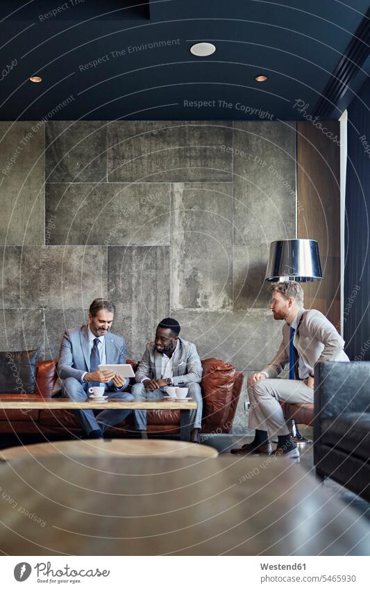 Drei Geschäftsleute sitzen mit einem Tablett in der Hotellobby geschäftlich Geschäftsleben Geschäftswelt Geschäftsperson Geschäftspersonen Geschäftsfreund