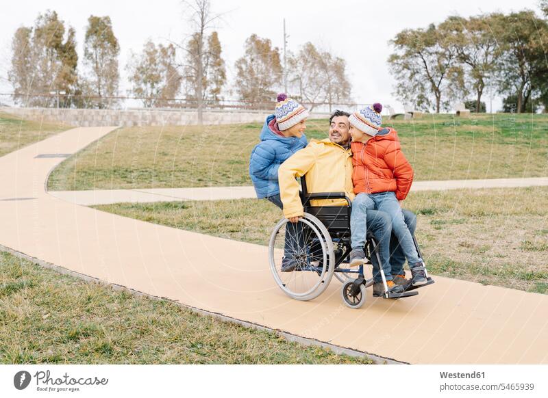 Verspielter Mann mit aufgeregten Söhnen im Rollstuhl auf einem Fußweg im Park Farbaufnahme Farbe Farbfoto Farbphoto Spanien Freizeitbeschäftigung Muße Zeit