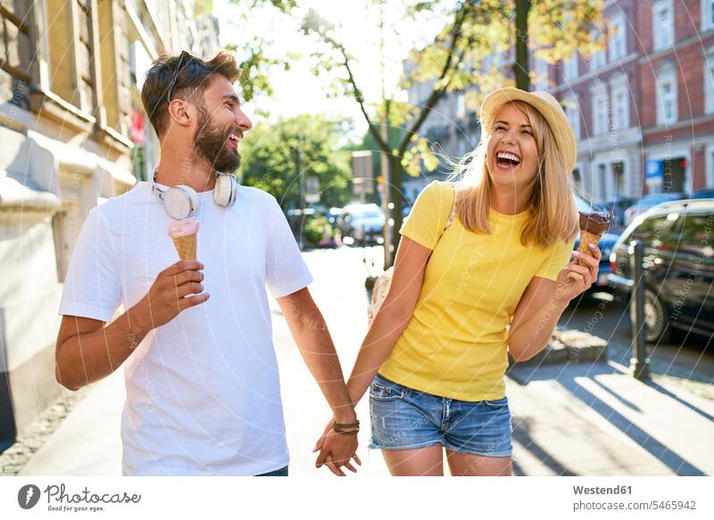 Glückliches junges Paar genießt Eiscreme in der Stadt Touristen Hüte T-Shirts KFZ Verkehrsmittel Automobil Autos PKW PKWs Wagen Kopfhoerer gehend geht