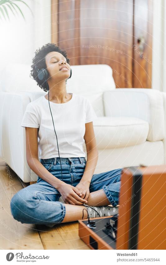 Junge Frau sitzt auf dem Boden, hört Musik vom Plattenspieler und benutzt Kopfhörer auf dem Boden sitzen auf dem Boden sitzend Schallplatte Vinyl Schallplatten