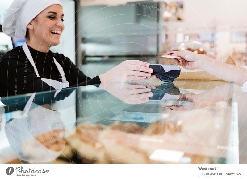 Glücklicher Bäcker erhält kontaktlose Zahlung per Kreditkarte vom Kunden in der Bäckerei Farbaufnahme Farbe Farbfoto Farbphoto Innenaufnahme Innenaufnahmen