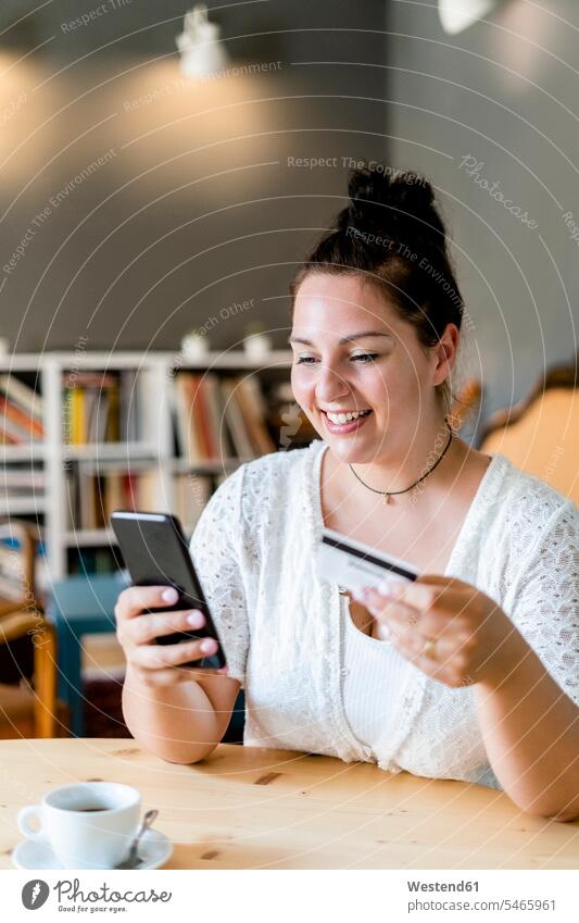 Lächelnde üppige Frau beim Online-Shopping über Handy im Café Farbaufnahme Farbe Farbfoto Farbphoto Innenaufnahme Innenaufnahmen innen drinnen Millennials