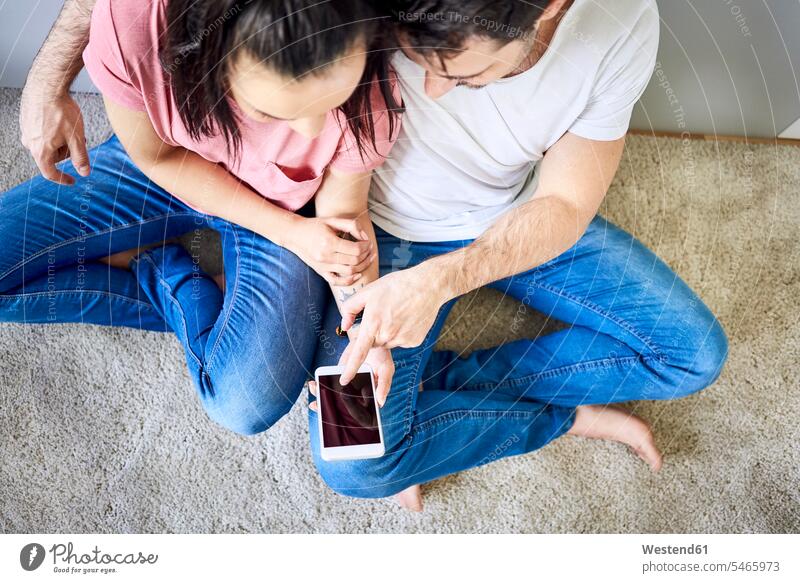Paare, die gemeinsam ein Smartphone benutzen sitzen sitzend sitzt Pärchen Partnerschaft Boden Böden Boeden iPhone Smartphones Gemeinsam Zusammen Miteinander