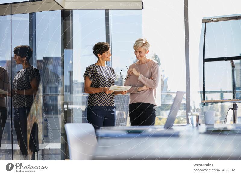 Zwei lächelnde Geschäftsfrauen, die ein Dokument am Fenster im Büro besprechen Businesswomen Businessfrauen Businesswoman Office Büros arbeiten Arbeit
