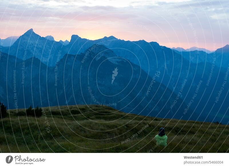 Österreich, Tirol, Wanderer sitzt in der Abenddämmerung auf einer Almwiese Bergwiese Bergwiesen Wanderin Wanderinnen Dämmerung Daemmerung sitzen sitzend Wiese