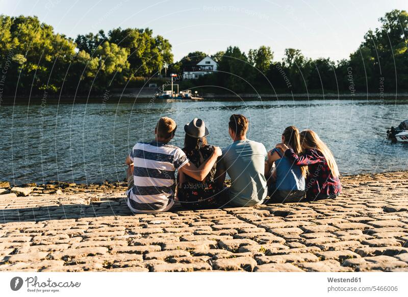 Gruppe von Freunden sitzt am Wasser und schaut hinaus sitzen sitzend Gruppe von Menschen Menschengruppe umarmen Umarmung Umarmungen Arm umlegen Freundschaft