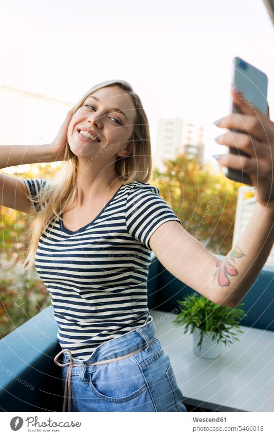 Lächelnde junge Frau macht ein Selfie auf dem Balkon Selfies Balkone Handy Mobiltelefon Handies Handys Mobiltelefone lächeln weiblich Frauen Telefon