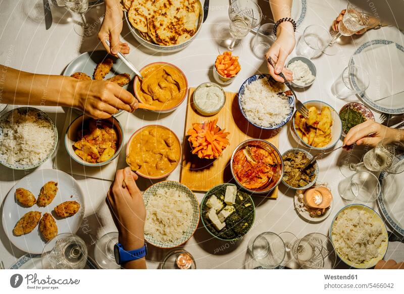 Hände von Menschen, die gemeinsam um einen mit indischem Essen gedeckten Tisch essen Innenaufnahme Innenaufnahmen innen drinnen Draufsicht von oben Aufsicht