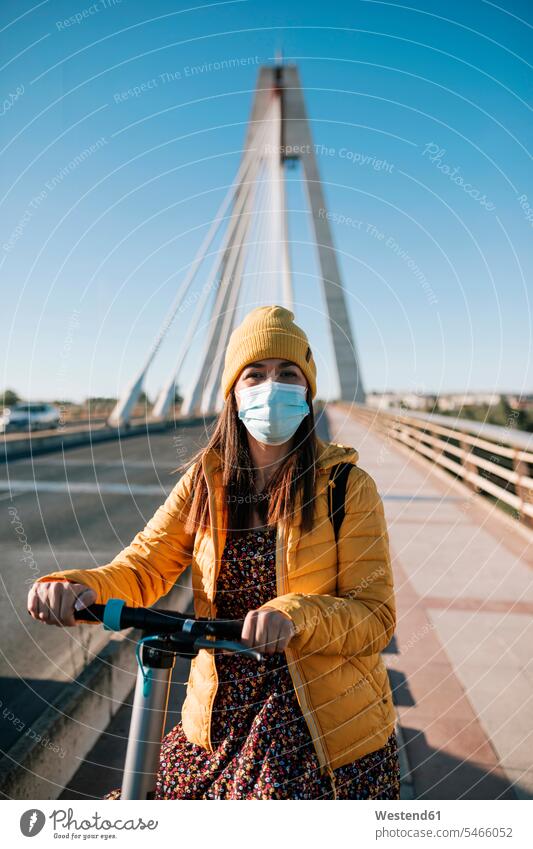 Frau mit schützender Gesichtsmaske mit Elektroroller auf einer Brücke in der Stadt während COVID-19 Farbaufnahme Farbe Farbfoto Farbphoto Außenaufnahme außen