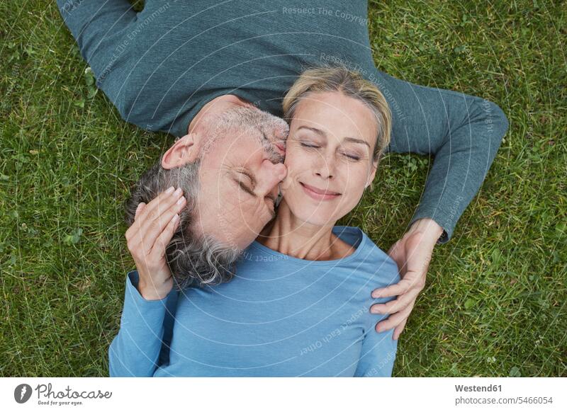 Draufsicht auf ein liebevolles reifes Paar, das im Gras liegt anfassen Berührung knuddeln schmusen Kuss Küsse entspannen relaxen entspanntheit relaxt freuen