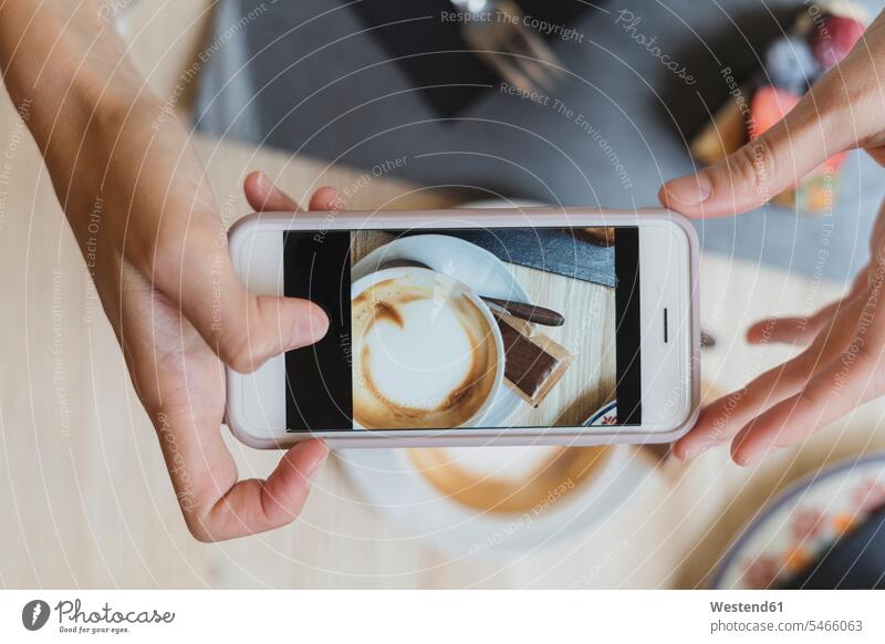 Draufsicht einer Frau in einem Cafe, die ein Handyfoto von Cappuccino macht Bilder Bildnis Fotos Tische Handies Handys Mobiltelefon Mobiltelefone Displays Muße