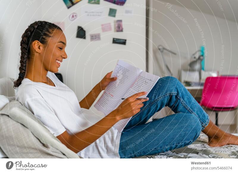 Teenager-Mädchen liest im Schulheft und sitzt zu Hause auf dem Bett Farbaufnahme Farbe Farbfoto Farbphoto Innenaufnahme Innenaufnahmen innen drinnen Tag