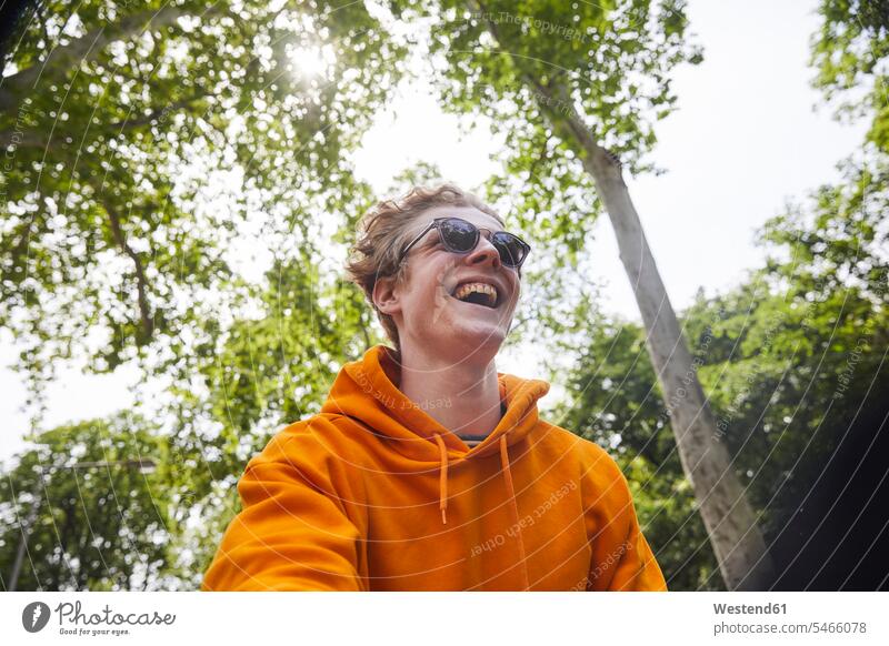 Porträt eines lachenden jungen Mannes mit Sonnenbrille und orangem Kapuzenhemd in der Natur Brillen Sonnenbrillen freuen witzig Muße Lifestyles Spass spassig