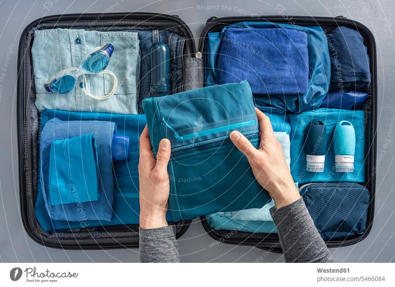 Draufsicht eines Mannes, der einen Koffer mit Kleidung und Schwimmbrille packt Reisegepäck Handtuecher Handtücher verreisen Jahreszeiten sommerlich Sommerzeit