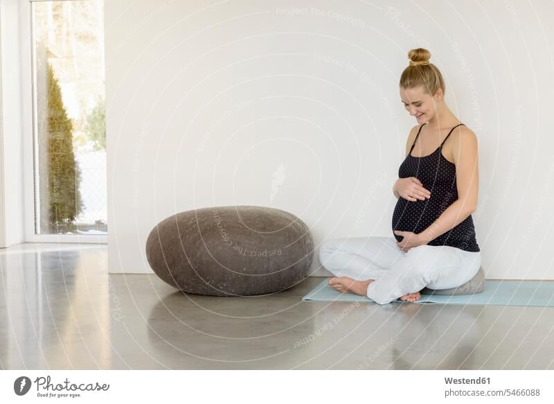 Lächelnde schwangere Frau sitzt auf einer Yogamatte Schwangere lächeln sitzen sitzend Yoga-Übungen Yogauebungen Yogaübungen Jogauebung Jogauebungen weiblich