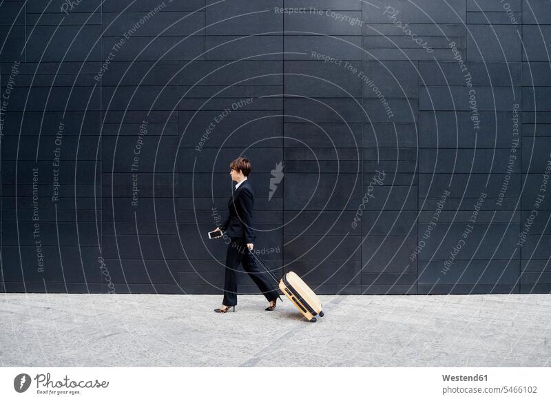 Geschäftsfrau mit Koffer geht auf dem Bürgersteig an einem modernen Gebäude in der Stadt Farbaufnahme Farbe Farbfoto Farbphoto Außenaufnahme außen draußen