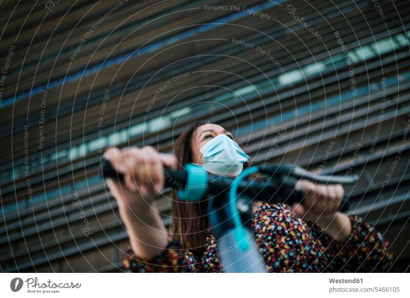 Reife Frau mit schützender Gesichtsmaske mit Elektroroller gegen Bauen während Coronavirus-Krise Farbaufnahme Farbe Farbfoto Farbphoto Außenaufnahme außen