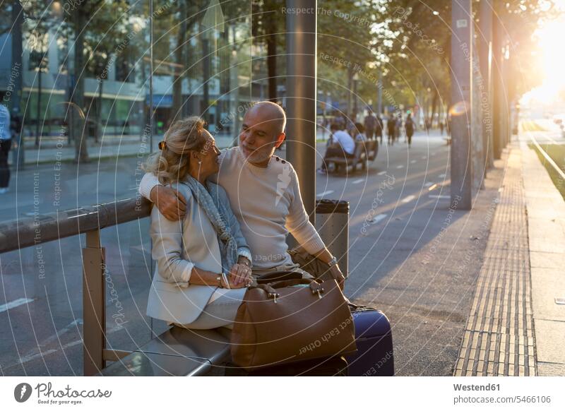 Spanien, Barcelona, älteres Paar mit Gepäck sitzt an der Straßenbahnhaltestelle in der Stadt bei Sonnenuntergang Straßenbahnhaltestellen staedtisch städtisch
