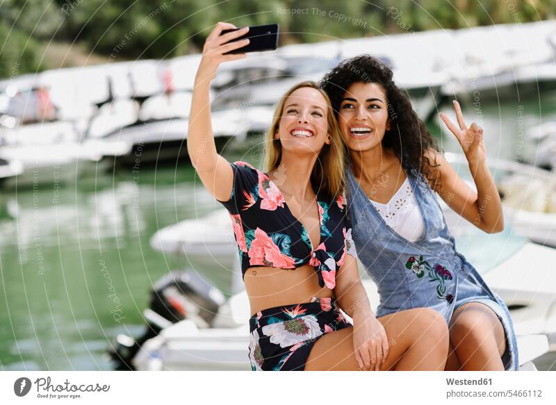 Zwei glückliche junge Frauen machen ein Selfie am Yachthafen im Sommer Freundinnen Handy Mobiltelefon Handies Handys Mobiltelefone Jachthafen Jachthäfen