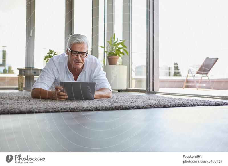 Reifer Mann liegt auf Teppich zu Hause mit Tablette liegen liegend Männer männlich Zuhause daheim entspannt entspanntheit relaxt Teppiche Tablet Computer