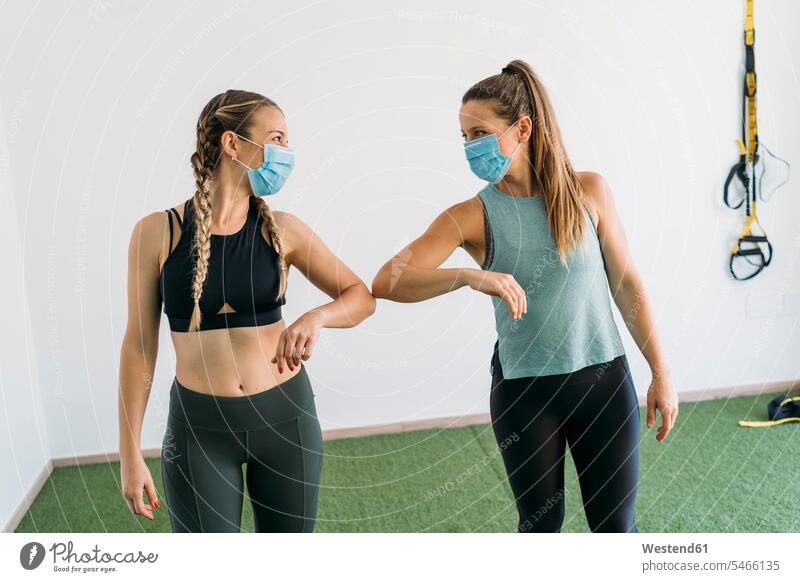 Zwei sportliche Frauen mit Gesichtsmasken, die im Fitnessclub den Ellbogen anstoßen Leute Menschen People Person Personen Europäisch Kaukasier kaukasisch 2