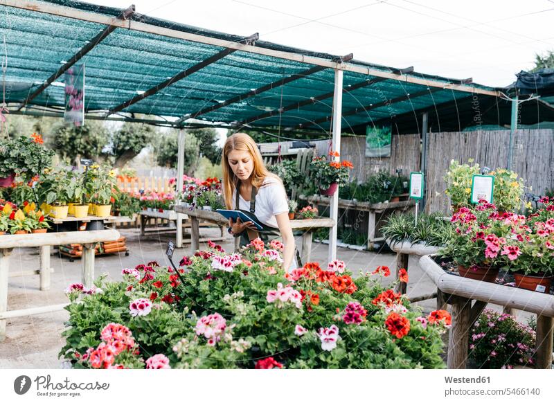 Weiblicher Arbeiter in einem Gartencenter mit einem Tablet, das sich um Blumen kümmert Job Berufe Berufstätigkeit Beschäftigung Jobs stehend steht Gartenarbeit