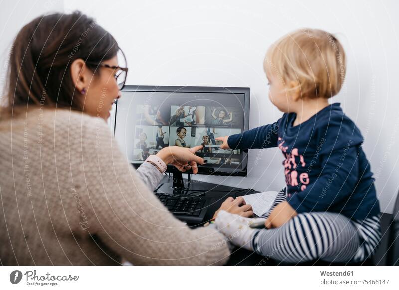 Mutter mit kleiner Tochter sitzt auf dem Schreibtisch und schaut auf den Computerbildschirm sitzen sitzend Zuhause zu Hause daheim ansehen Mami Mutti Mütter