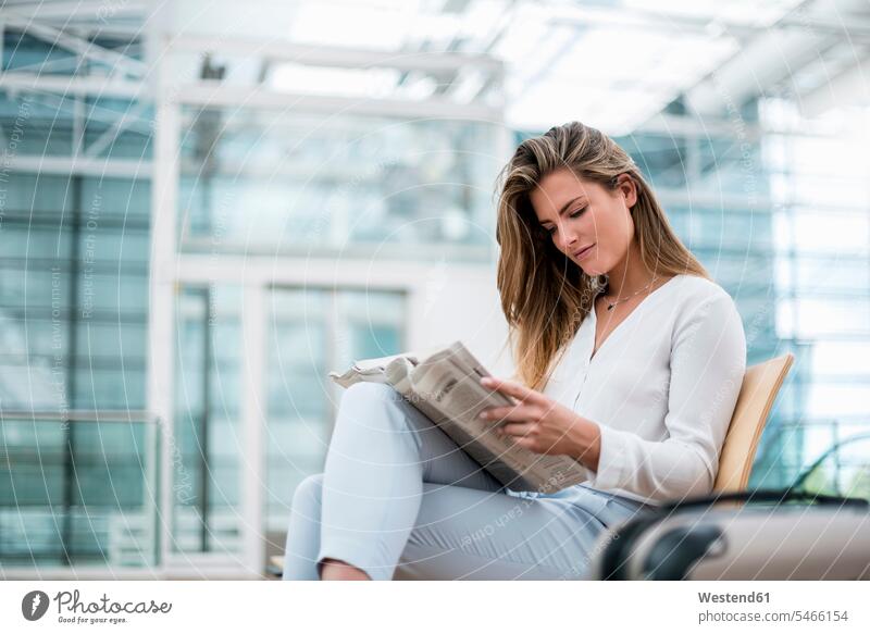 Junge Geschäftsfrau sitzt mit Koffer im Freien und liest Zeitung Geschäftsfrauen Businesswomen Businessfrauen Businesswoman lesen Lektüre Zeitungen sitzen