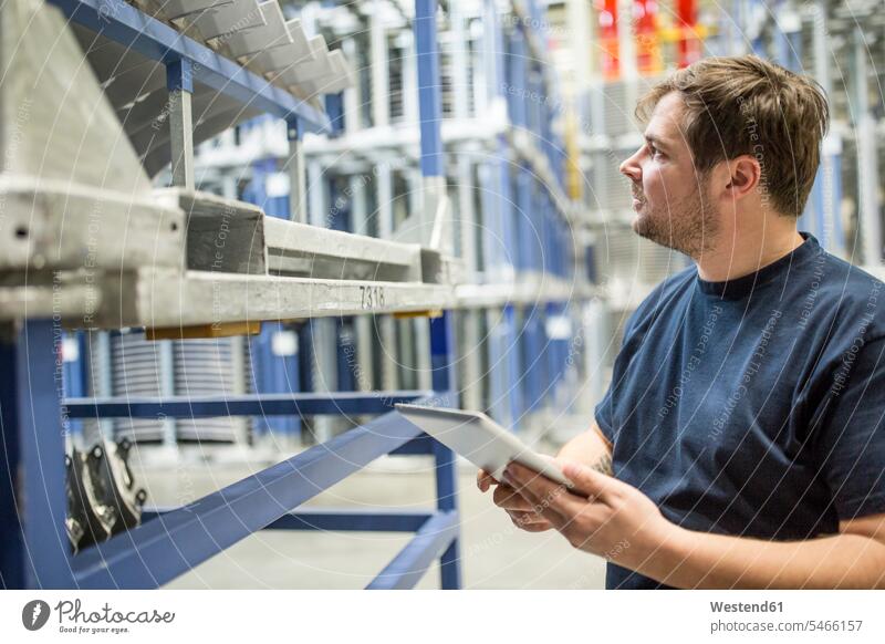 Arbeiter mit Tablette im Fabriklager Job Berufe Berufstätigkeit Beschäftigung Jobs T-Shirts Ablage Regale stehend steht Firma Gewerbe industriell Industrien