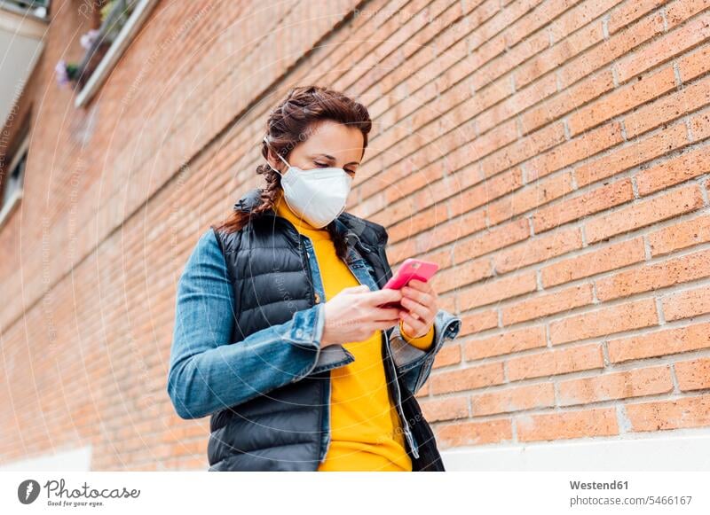 Frau, die ihr Gesicht mit einer Schutzmaske bedeckt und ein Smartphone benutzt Telekommunikation telefonieren Handies Handys Mobiltelefon Mobiltelefone Gesund