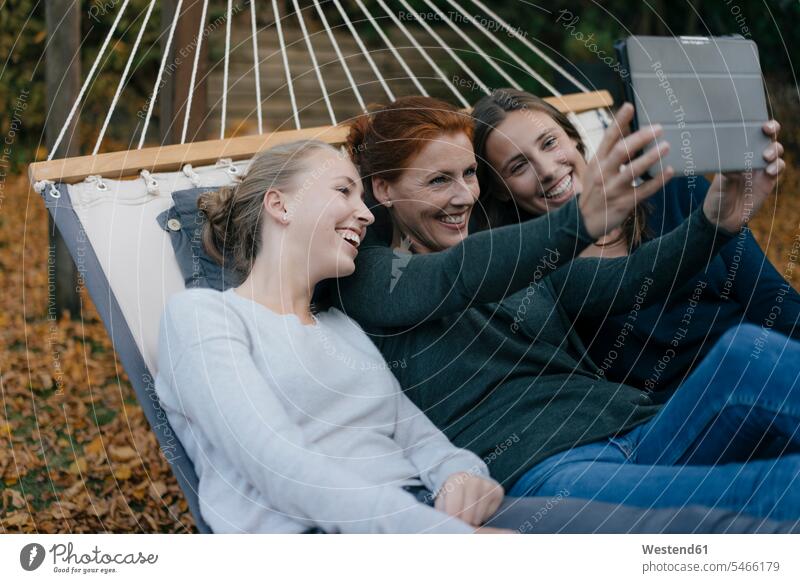 Glückliche Mutter mit zwei Teenager-Mädchen liegen in der Hängematte im Garten im Herbst mit Tablet liegend liegt Hängematten Mami Mutti Mütter Mama Tochter