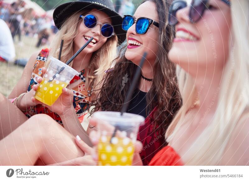 Freunde trinken Saft und sitzen während des Musikfestivals auf der Wiese Spaß Spass Späße spassig Spässe spaßig Saefte Säfte fröhlich Fröhlichkeit Frohsinn