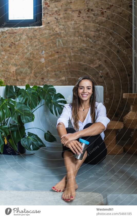 Lächelnde Geschäftsfrau mit isoliertem Kaffeebecher auf dem Boden sitzend im Büro Portugal Farbaufnahme Farbe Farbfoto Farbphoto Geschäftsfrauen Businessfrau