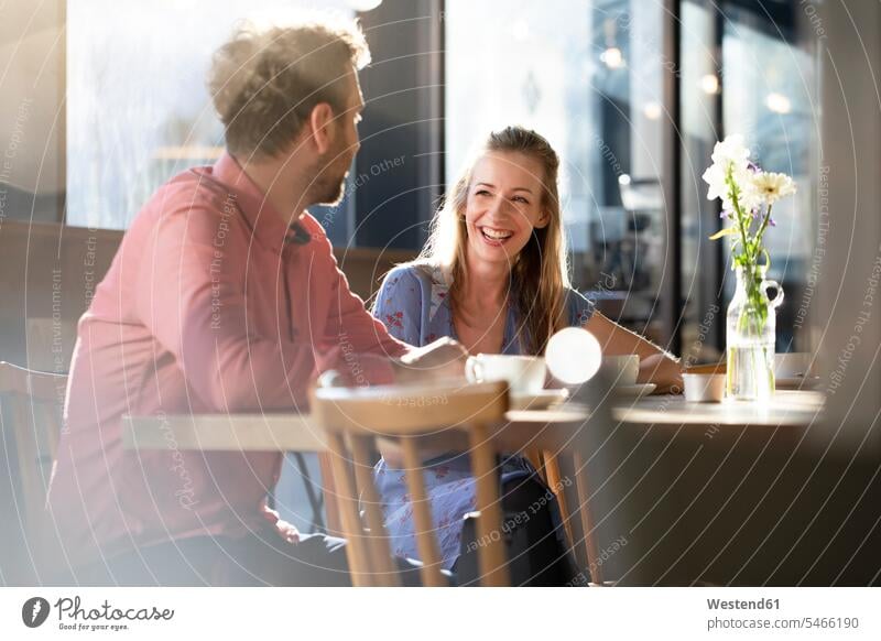 Lachende Frau und lachender Mann unterhalten sich am Tisch in einem Cafe Tische Flirt sitzend sitzt reden freuen Frohsinn Fröhlichkeit Heiterkeit Glück