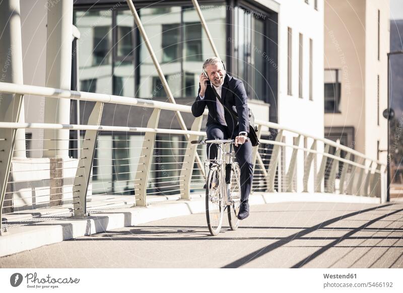 Lächelnde reifen Geschäftsmann mit Kopfhörer Fahrrad fahren auf einer Brücke in der Stadt Bruecken Brücken staedtisch städtisch lächeln Kopfhoerer Bikes
