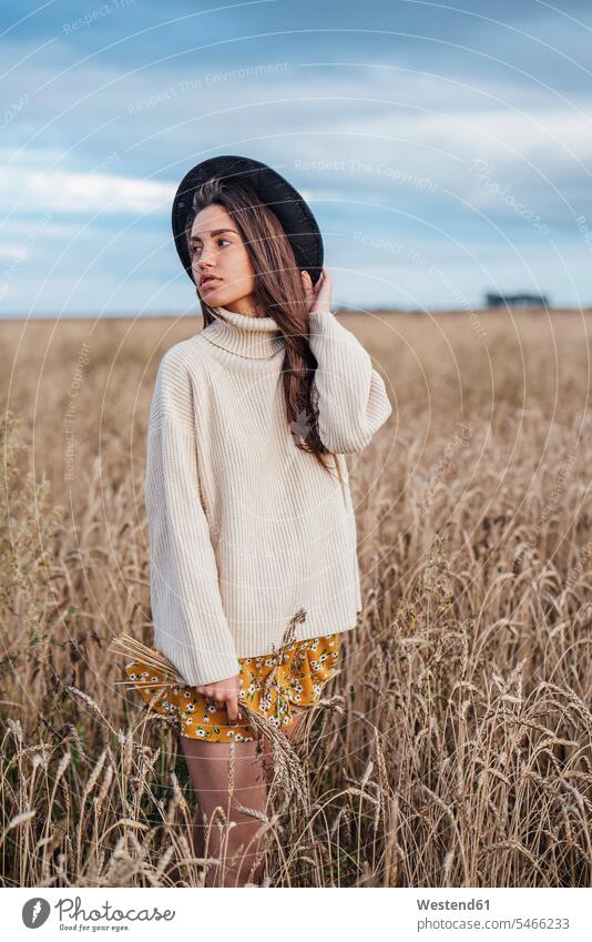 Porträt einer jungen Frau mit Hut und übergroßem Rollkragenpullover im Maisfeld stehend Hüte Kornfeld Getreidefeld Getreidefelder Kornfelder Feld Felder riesig