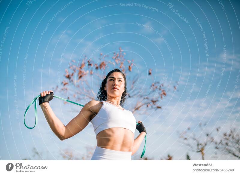 Selbstbewusste Sportlerin mit Widerstandsband gegen den Himmel an einem sonnigen Tag Farbaufnahme Farbe Farbfoto Farbphoto Außenaufnahme außen draußen im Freien