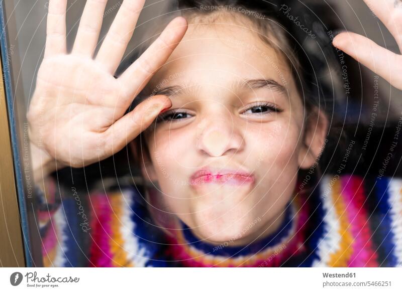 Porträt eines fröhlichen, verspielten Mädchens im gestreiften Pullover hinter einer Fensterscheibe glücklich Glück glücklich sein glücklichsein spielerisch