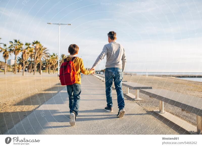Vater und Sohn spazieren an der Strandpromenade Papas Väter Vati Vatis Papis Beach Straende Strände Beaches Söhne gehen gehend geht Promenade Promenaden Eltern