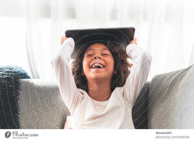 Porträt des kleinen Mädchens lachend auf dem Sofa mit digitalen Tablet in den Händen Tag Tageslichtaufnahme Tageslichtaufnahmen Tagesaufnahme am Tag