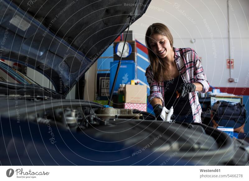 Junge Frau in Hemd und Handschuhen bei der Arbeit mit einem Auto in einer Reparaturwerkstatt, die den Motorölstand überprüft Leute Menschen People Person
