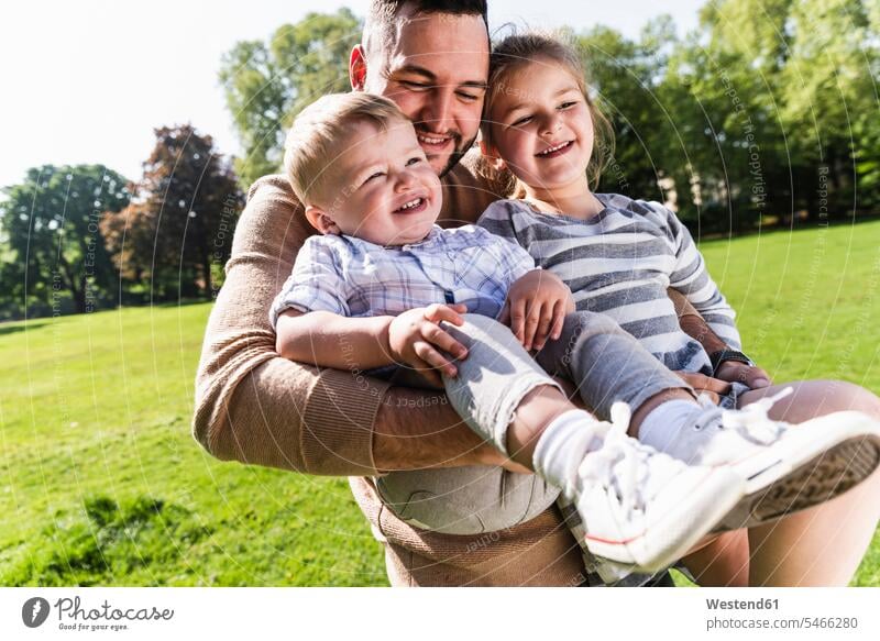 Glücklicher Vater trägt Kinder in einem Park Papas Väter Vati Vatis Papis Parkanlagen Parks glücklich glücklich sein glücklichsein tragen transportieren Familie