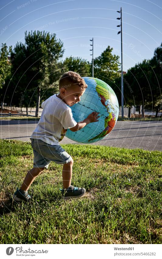Sorgloser Junge hält Globus, während er bei Sonnenschein auf Grasland läuft Farbaufnahme Farbe Farbfoto Farbphoto Spanien Freizeitbeschäftigung Muße Zeit