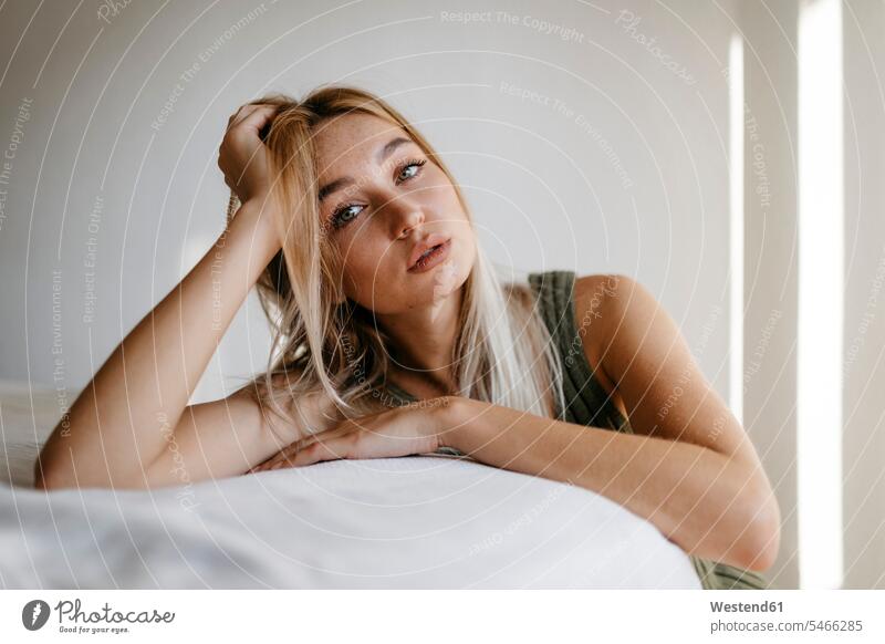 Verführerische junge Frau mit der Hand im Haar, die zu Hause das Bett anlehnt Farbaufnahme Farbe Farbfoto Farbphoto Innenaufnahme Innenaufnahmen innen drinnen